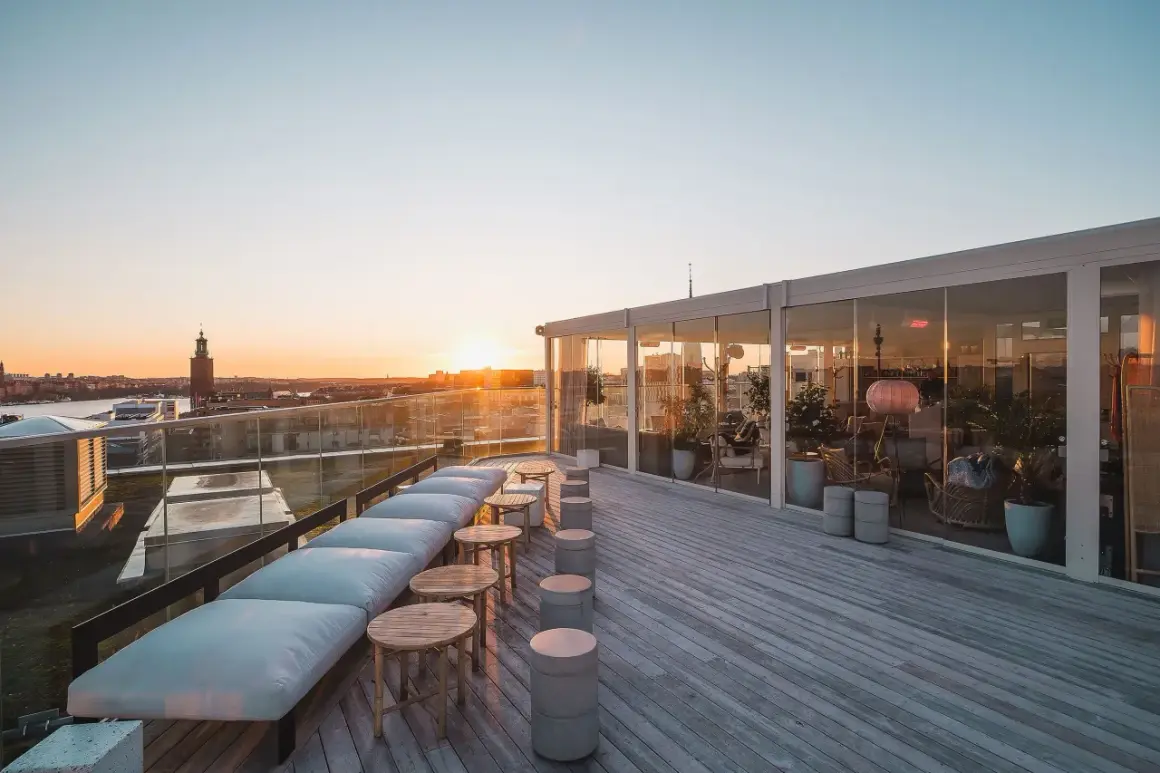 Takbar med utsikt över Stockholms silhuett vid solnedgången. En modern skyskrapa i Stockholm med sittplatser utomhus.