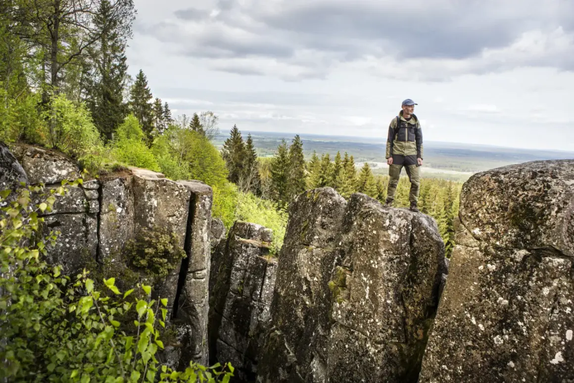 En man står på en klippa och njuter av utsikten över skog och landskap. En perfekt plats för att vandra i Europa.