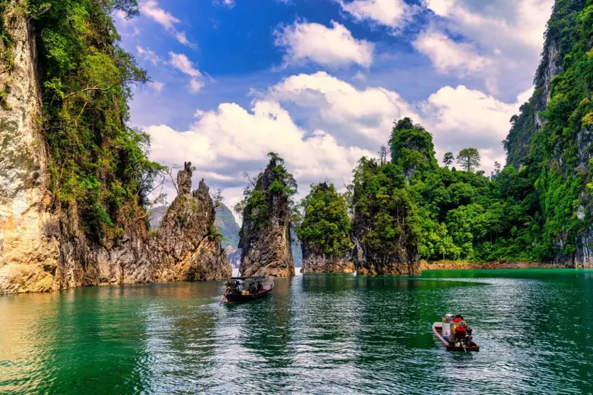 Khao Sok nationalpark med sina dramatiska kalkstensklippor och smaragdgröna vatten. Två små båtar glider fram på sjön.