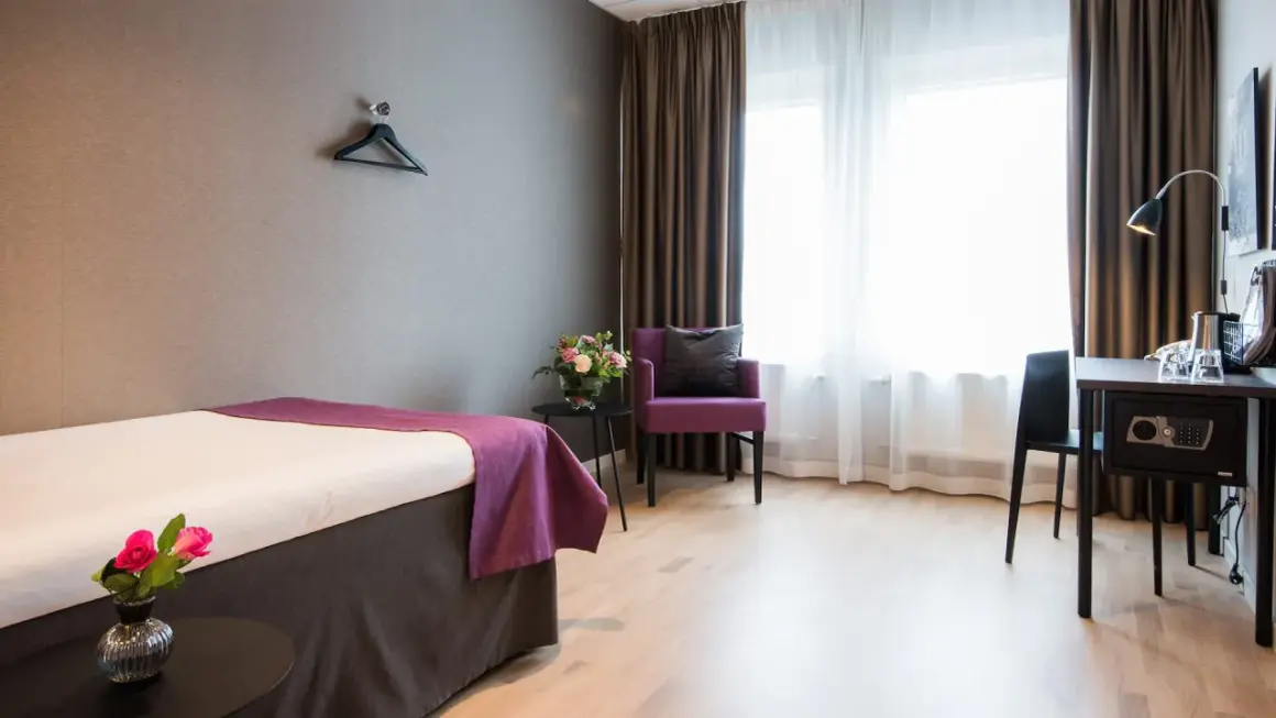 Ett hotellrum med en säng, en lila fåtölj och ett skrivbord. Perfekt för att sova på Arlanda.