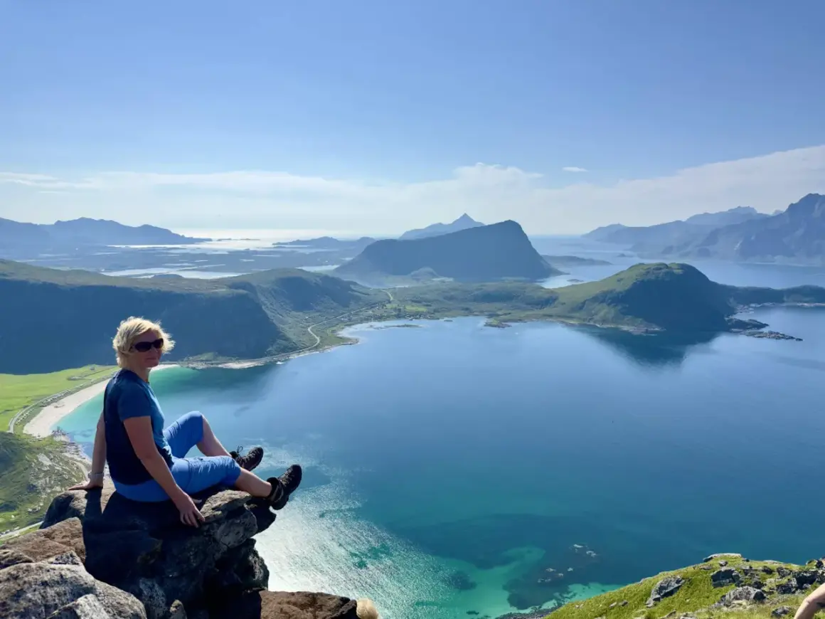 Kvinna sitter på klippavsats med fantastisk utsikt över fjordlandskap på Lofoten.
