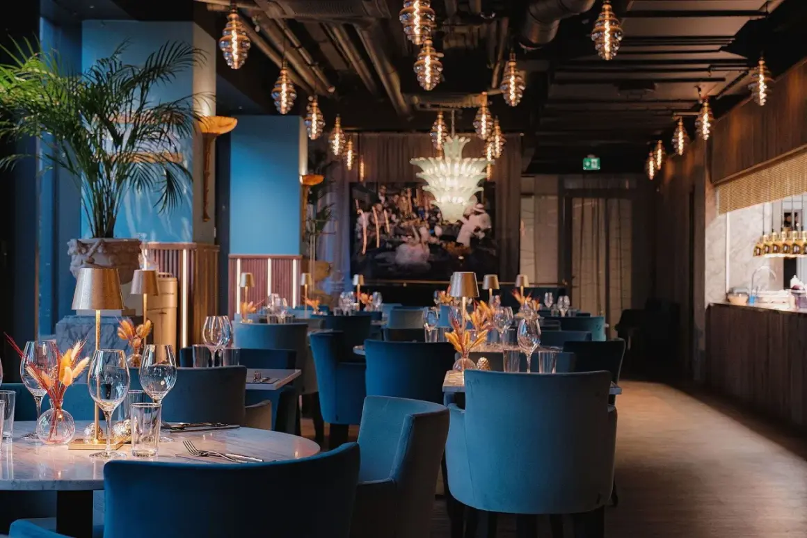Elegant pava restaurang med blå sammetsstolar, marmorbord och dekorativa lampor.