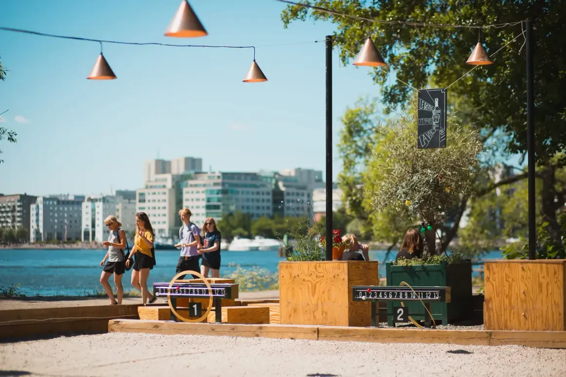 Vänner njuter av utomhusaktiviteter i Stockholm vid vattnet, med spel och stadens silhuett i bakgrunden.