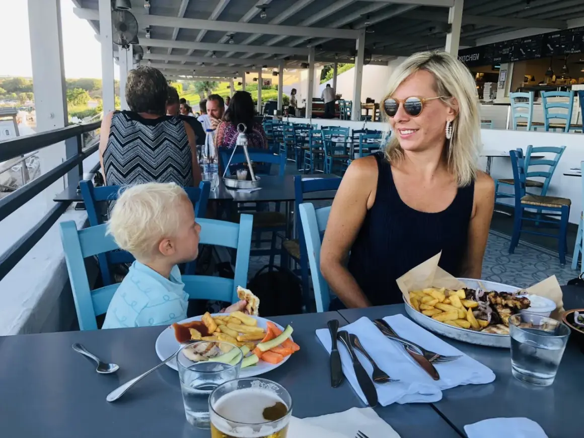 Familj njuter av en måltid på Costas Kitchen Kallithea. En kvinna ler, en pojke äter, och maten ser utsökt ut.