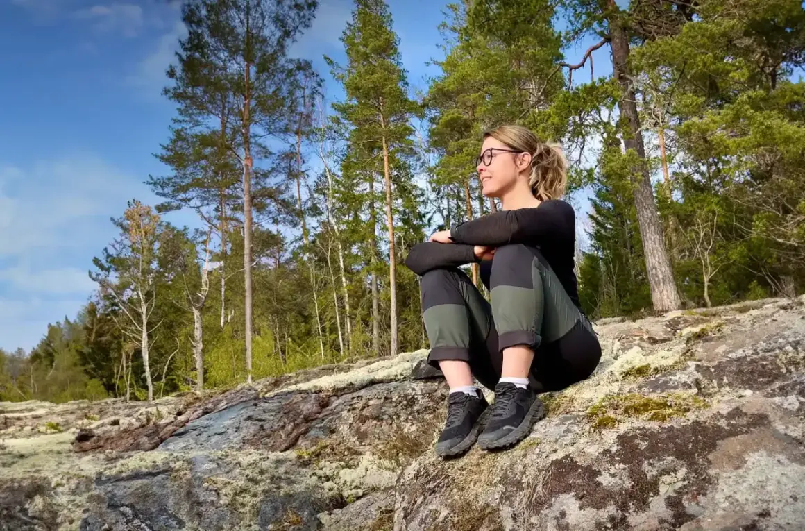 Kvinna sitter på en klippa i skogen, njuter av utsikten. Perfekt för utflykter Stockholm.