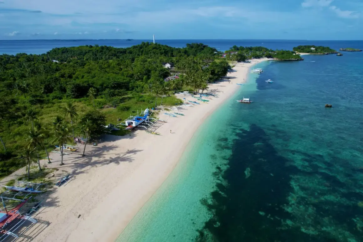 En vit sandstrand med palmer och traditionella filippinska båtar. Vattnet är turkost och klart, med en grönskande ö i bakgrunden. En idyllisk vy från Cebu, Filippinerna.
