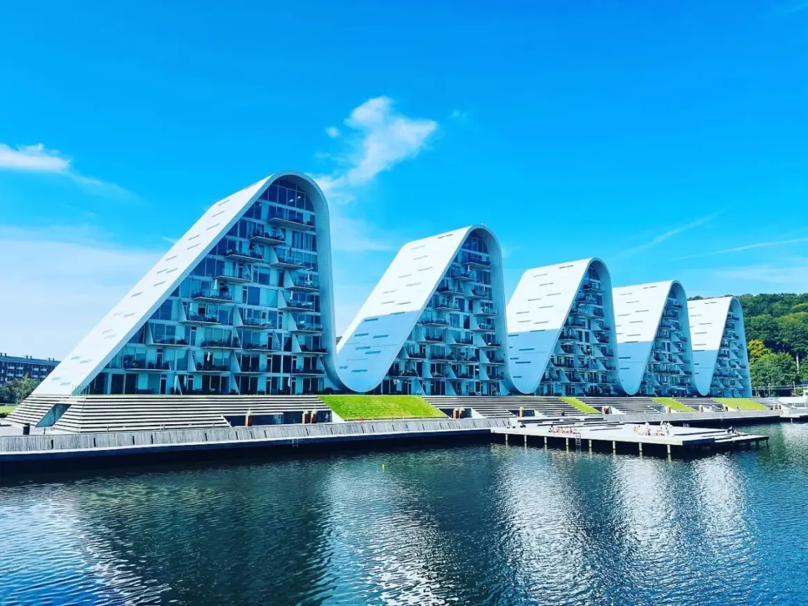 Vågformade byggnader vid vattnet i Vejle, Danmark. Moderna lägenheter med glasfasader och balkonger.