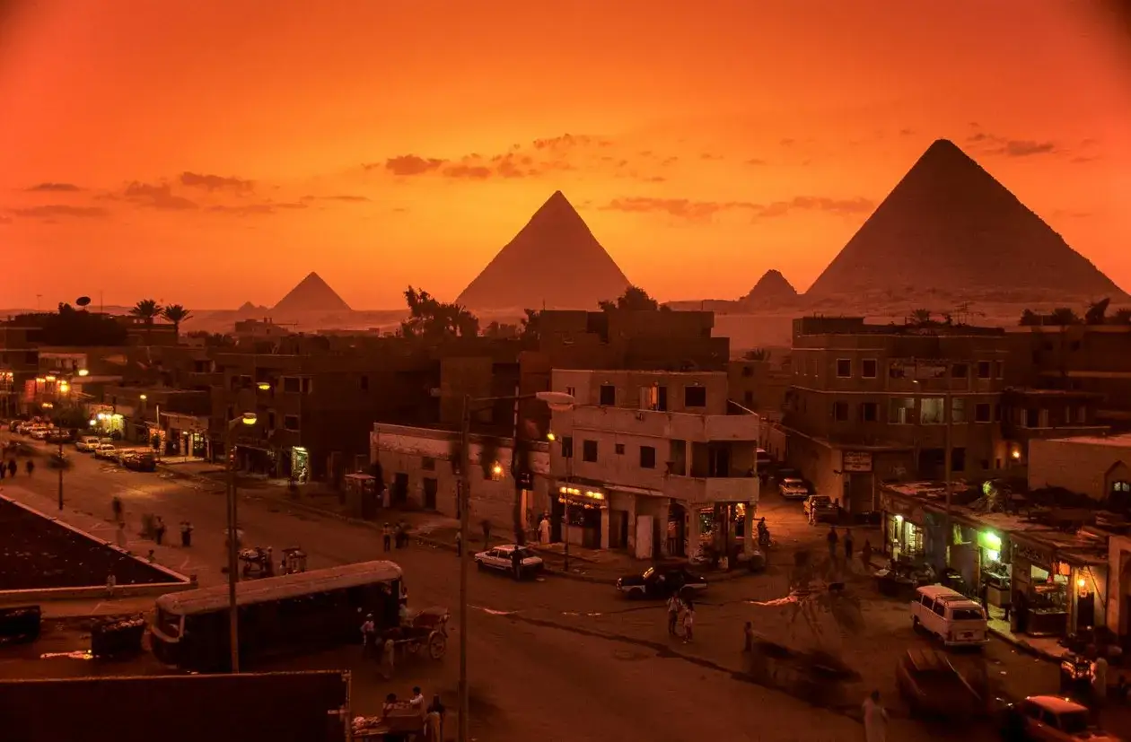 En stad i Egypten badar i ett orange skymningsljus, med pyramiderna i Egypten som majest&auml;tiska silhuetter i bakgrunden.