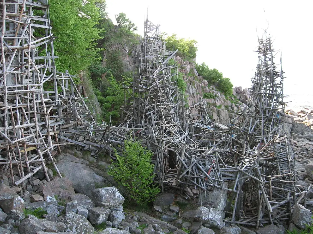 Lars Vilks Nimis, en skulptur av drivved och trä, reser sig mot en klippig kust.