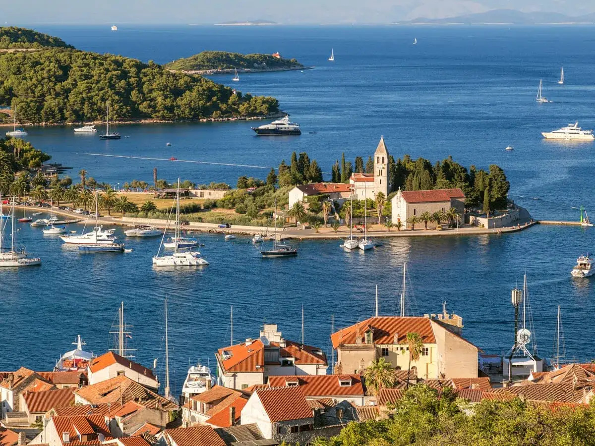 Vacker vy &ouml;ver en hamn i Kroatien med segelb&aring;tar, kyrka och gr&ouml;na kullar.