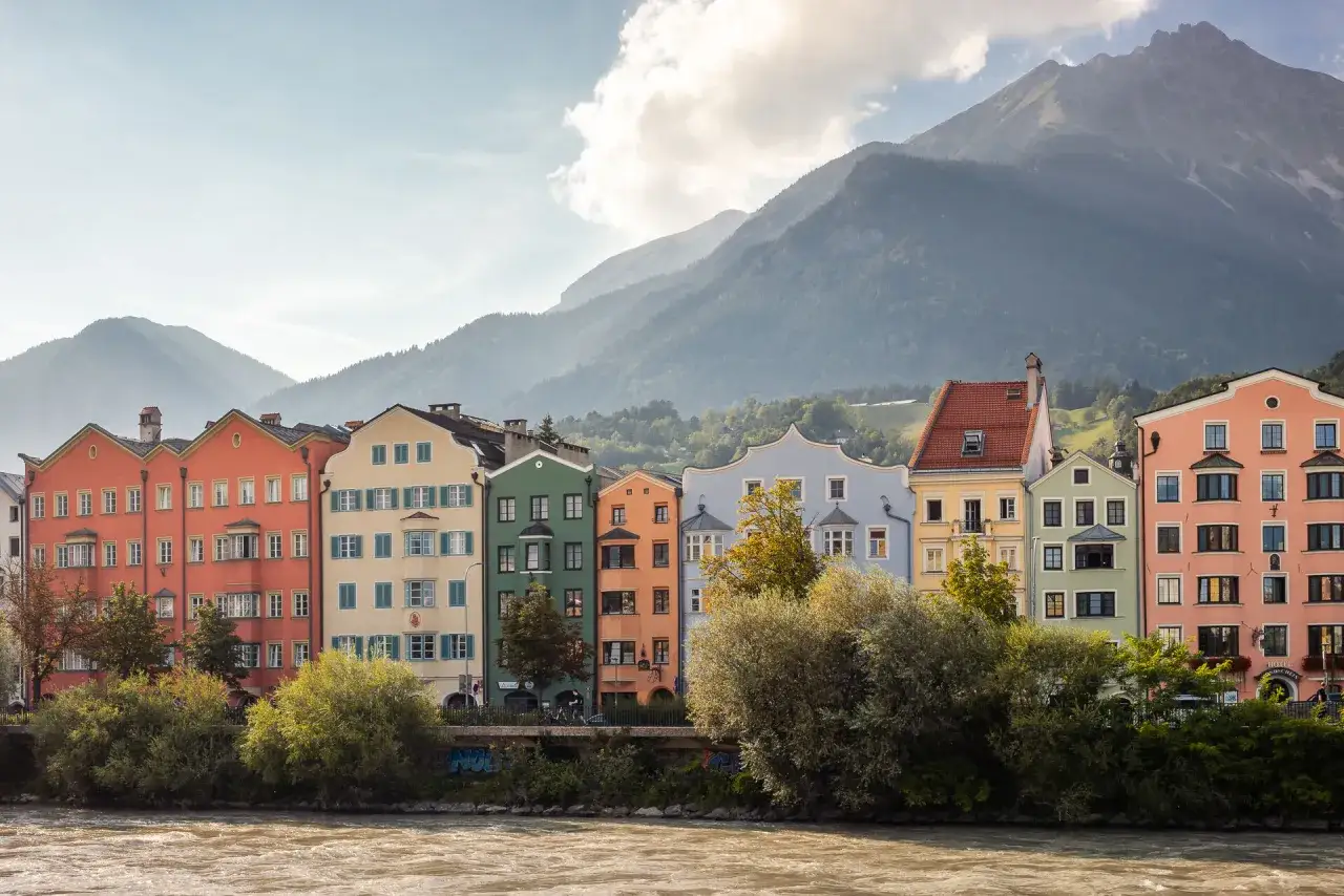 F&auml;rgglada hus l&auml;ngs en flod, med berg i bakgrunden. En vy som p&aring;minner om Zell am See.
