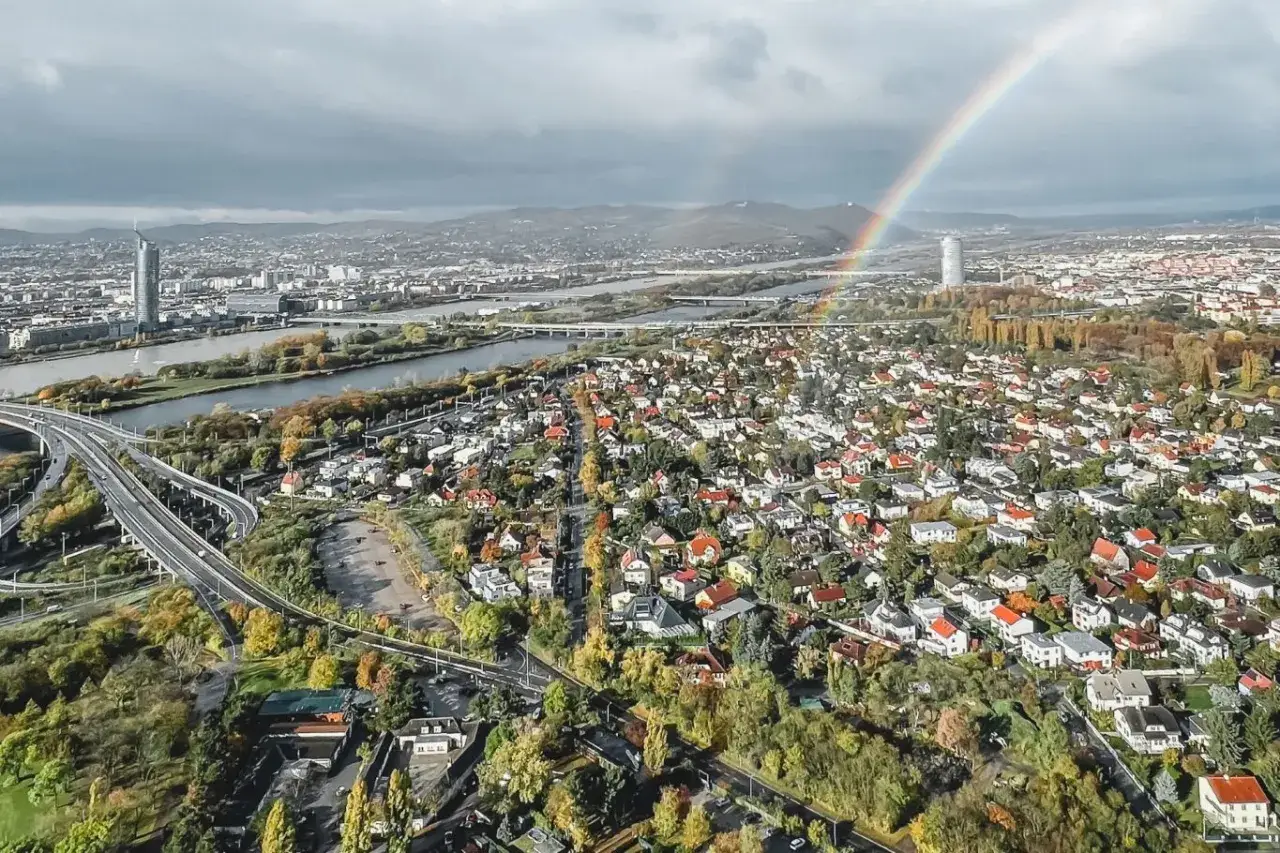 Vacker regnbåge över Wiens takåsar och Donau. En vy värd att se i Wien, med moderna skyskrapor och charmiga villakvarter.