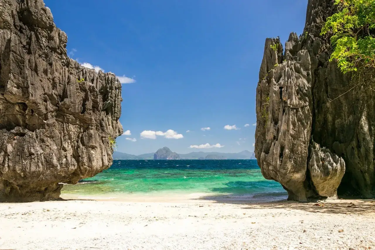 En vit sandstrand med turkost vatten och dramatiska klippformationer på Palawan, Filippinerna.