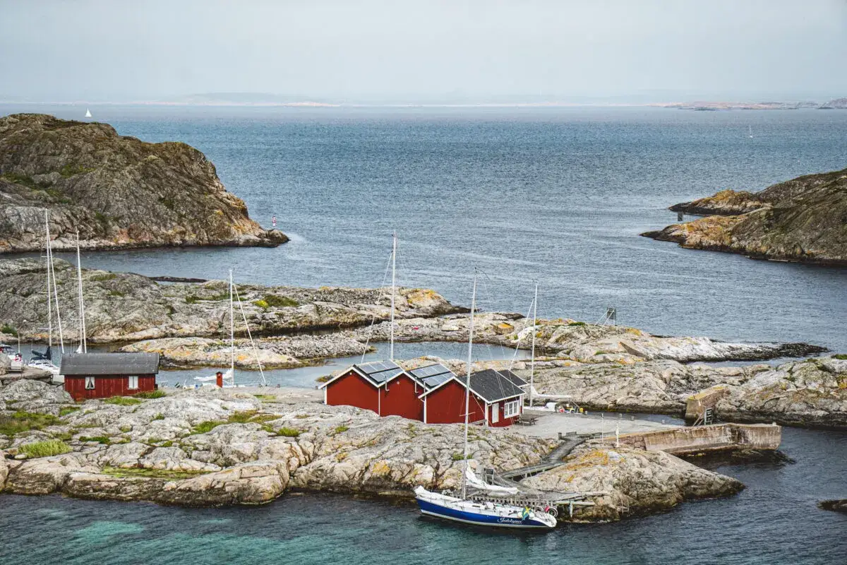 Röda sjöbodar och segelbåtar på en klippig ö. En idyllisk vy som passar perfekt för en bilsemester i Sverige.