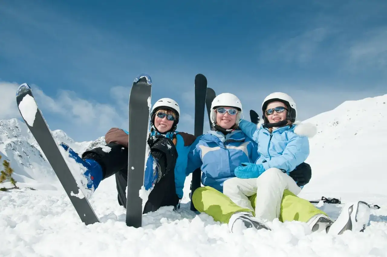 Glad familj på skidresa i Alperna. De sitter i snön med skidorna redo för mer åkning.