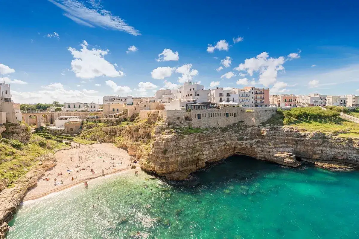Vackra vita hus klättrar uppför klipporna vid Polignano a Mare, med en solig strand och turkost vatten.