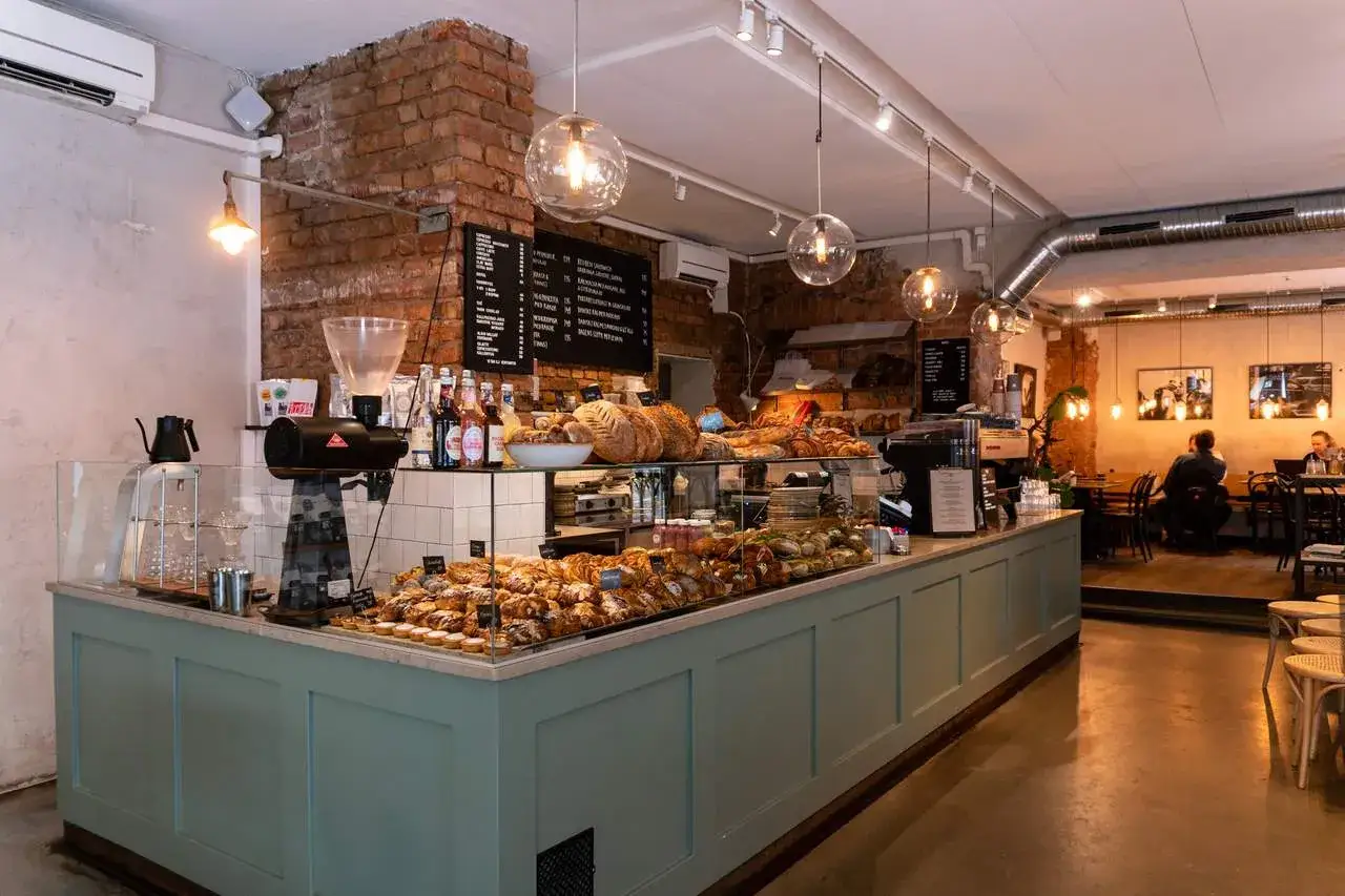 Ett mysigt café i Stockholm med en disk fylld av nybakade godsaker och bröd. Varm belysning och tegelväggar skapar en inbjudande atmosfär.