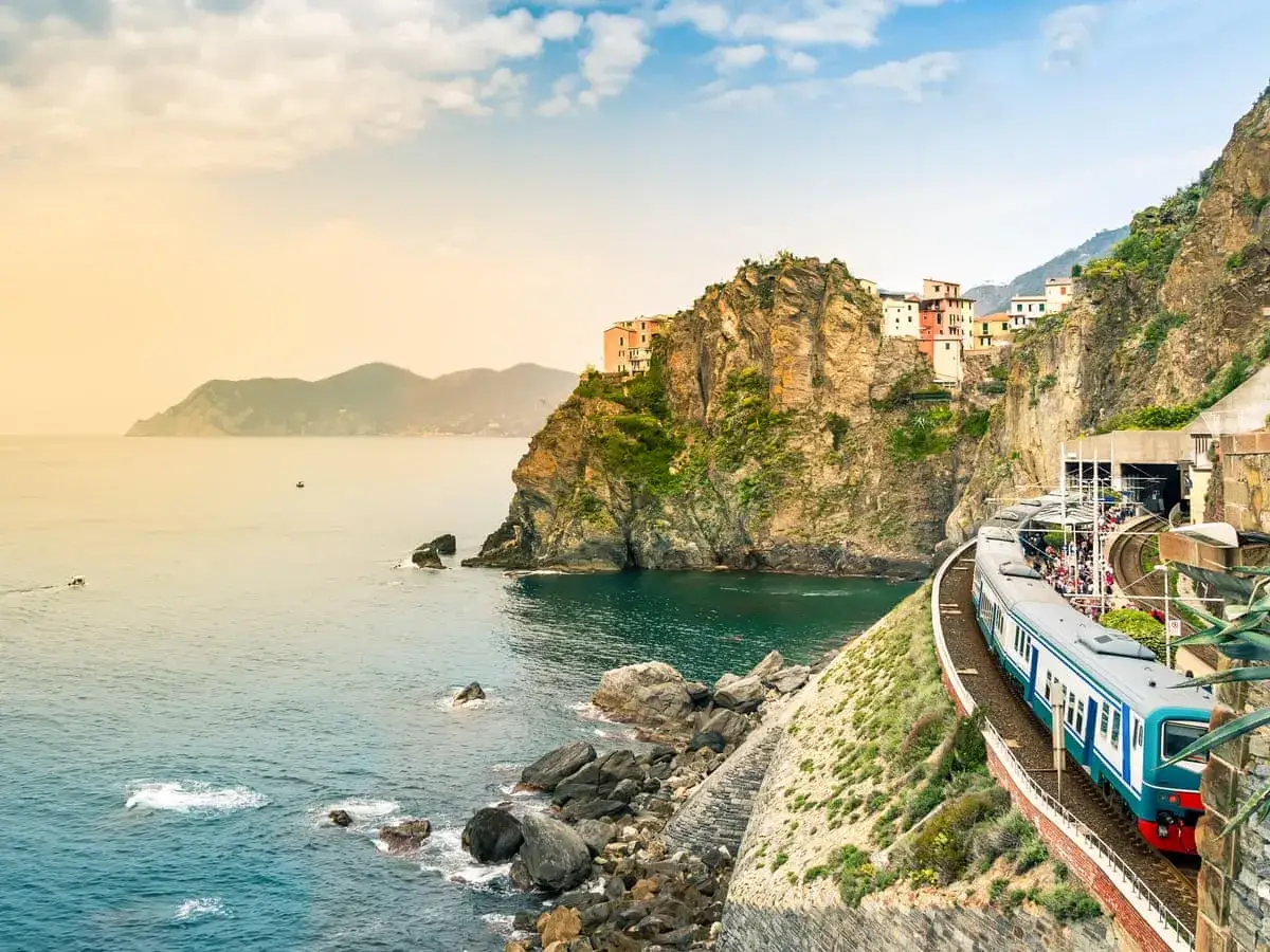 Ett tåg i Italien färdas längs en dramatisk kustlinje med färgglada hus på klipporna.