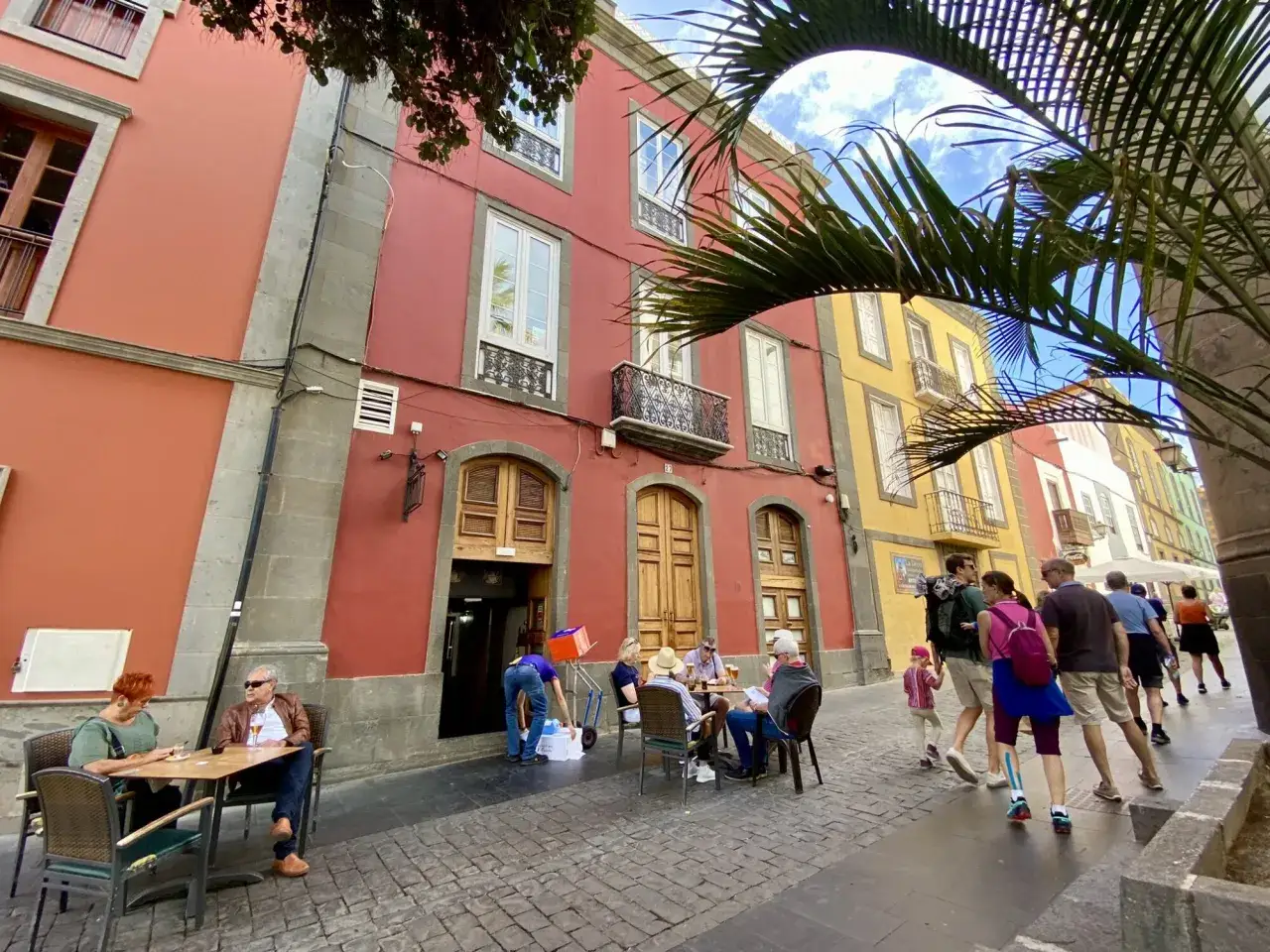 Färgstarka hus i Las Palmas gamla stan. Människor sitter vid bord utomhus och promenerar på kullerstensgatan.