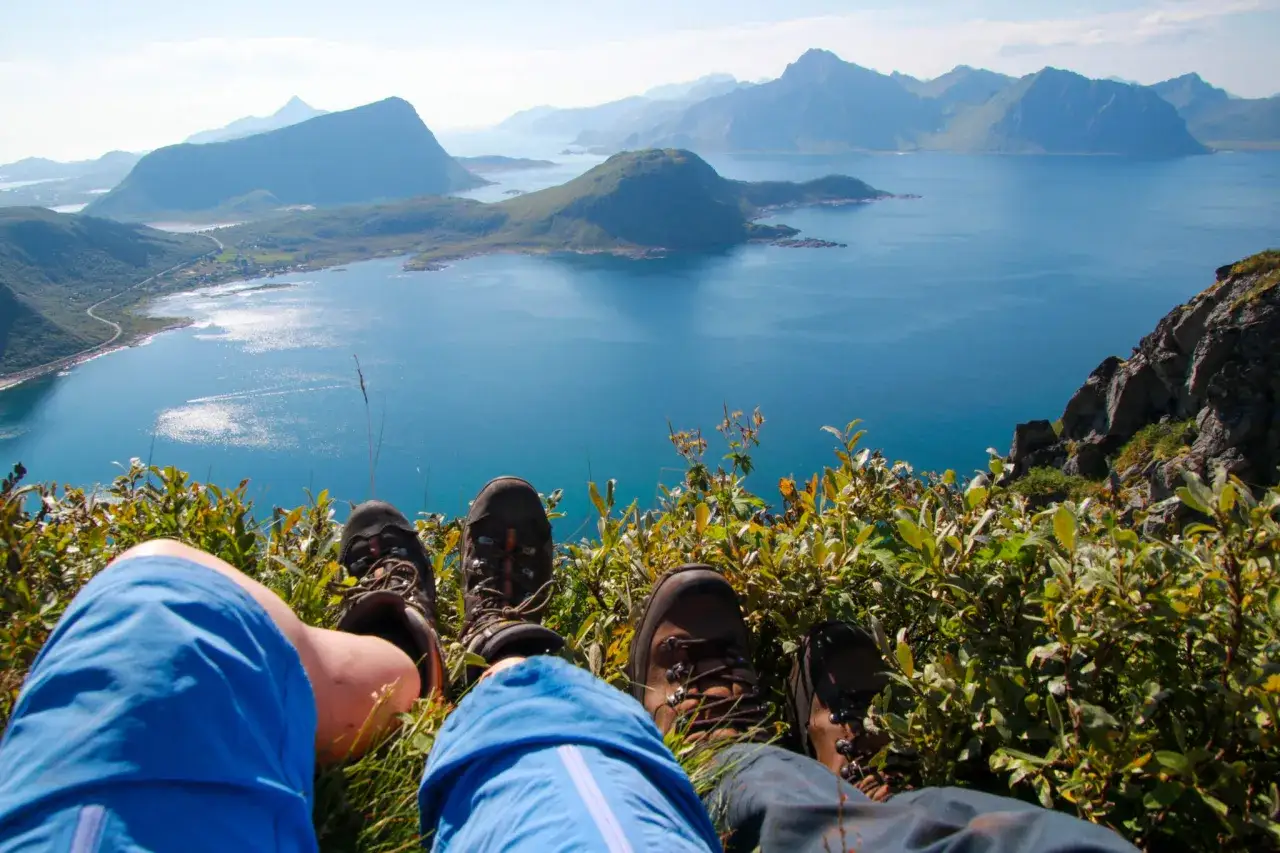 Vandringsst&ouml;vlar vilar p&aring; en gr&ouml;n sluttning med en fantastisk utsikt &ouml;ver Lofoten. Mannen njuter av tystnaden och den storslagna naturen.