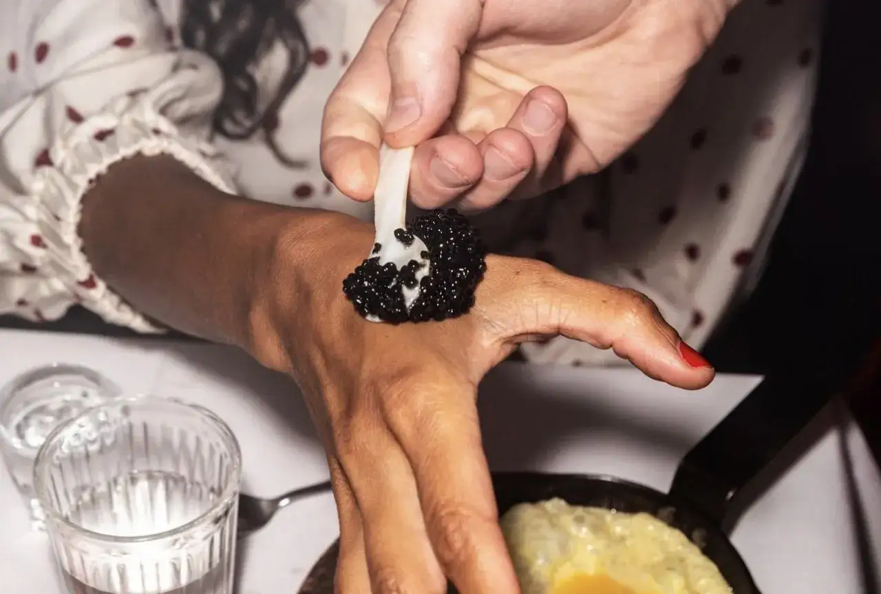 En hand lägger kaviar på en annan hand som en del av en unik matupplevelse på restaurang Punk Royale.