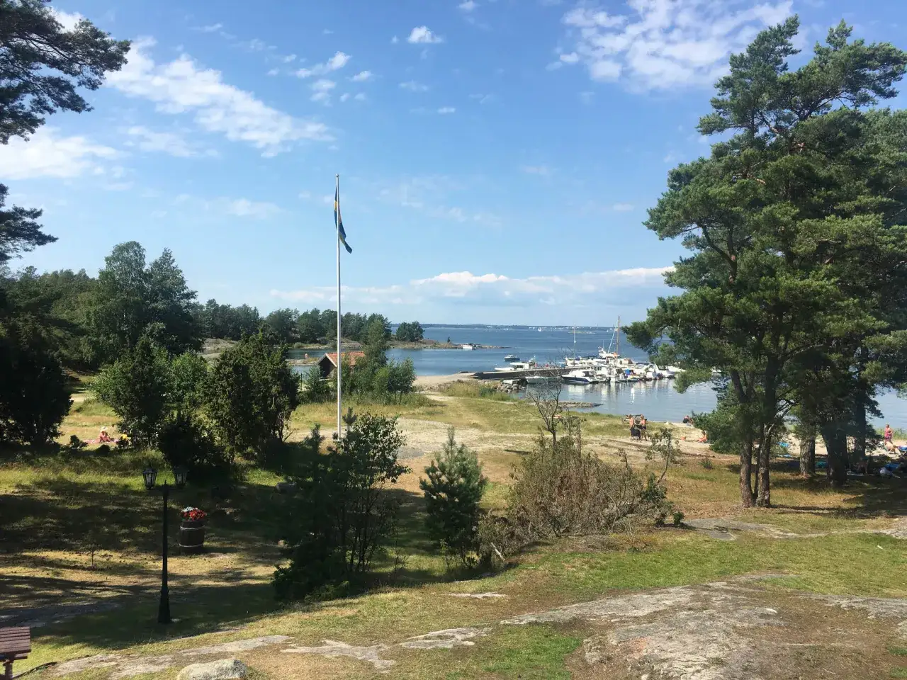 En solig dag vid vattnet, med båtar i hamnen och människor som njuter av sommaren. Ett perfekt utflyktsmål Stockholm.