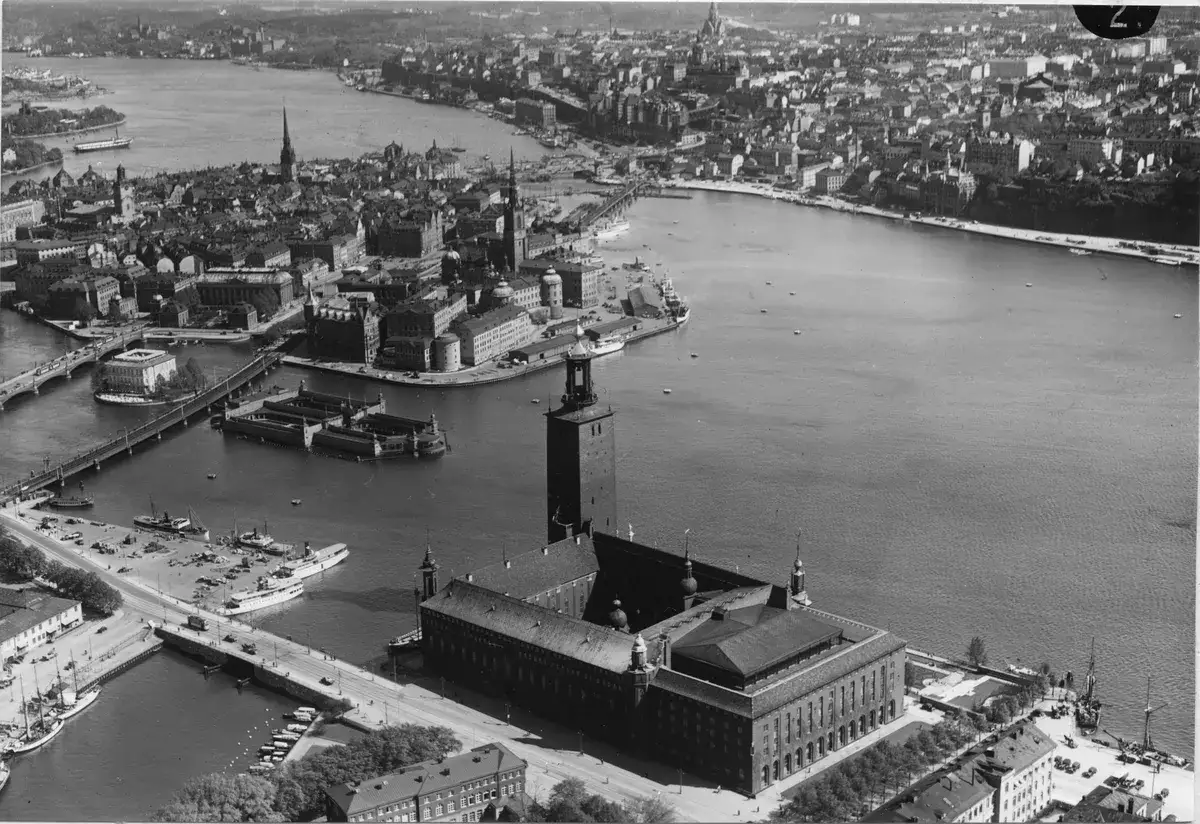 Vy över Stockholm med Stadshuset, en imponerande skyskrapa, som dominerar bilden vid vattnet.