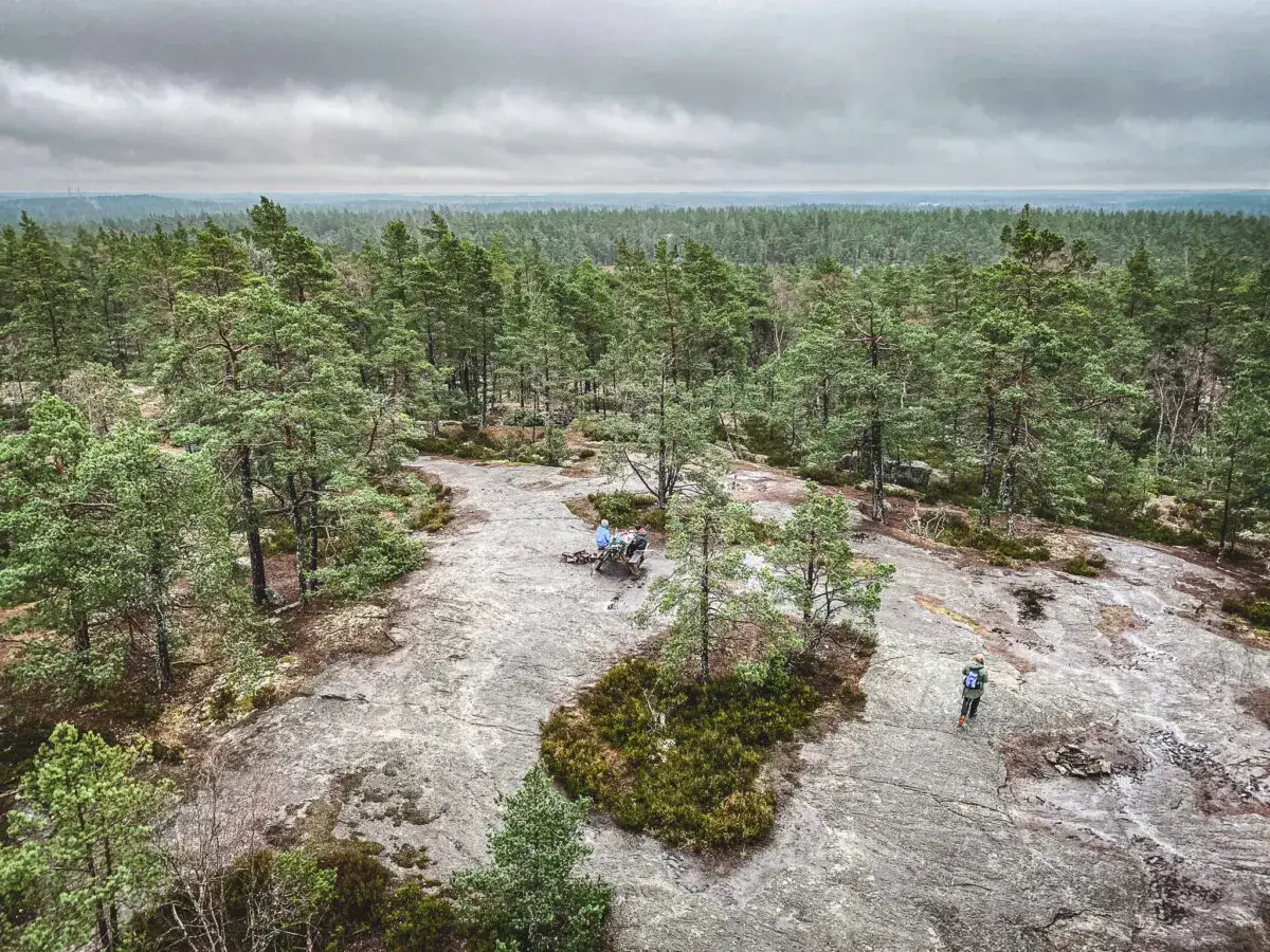 Vacker utsikt över paradiset naturreservat med skog och klippor. Två personer sitter vid ett bord, en vandrare går på klippan.