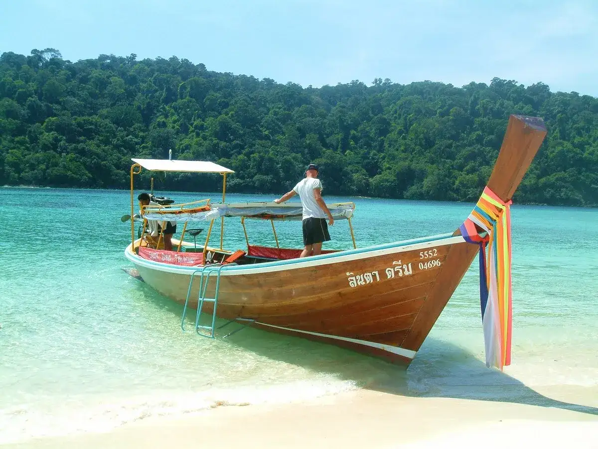En traditionell longtailbåt väntar vid stranden, redo för utflykter på Koh Lanta.