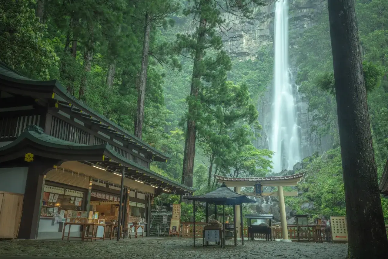 Vacker vy av Kumano Kodo med ett tempel och en imponerande vattenfall i en frodig skog.