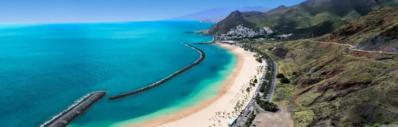 Vacker strand med turkost vatten och berg i bakgrunden. En dr&ouml;m f&ouml;r alla som planerar sin flygtid Teneriffa.