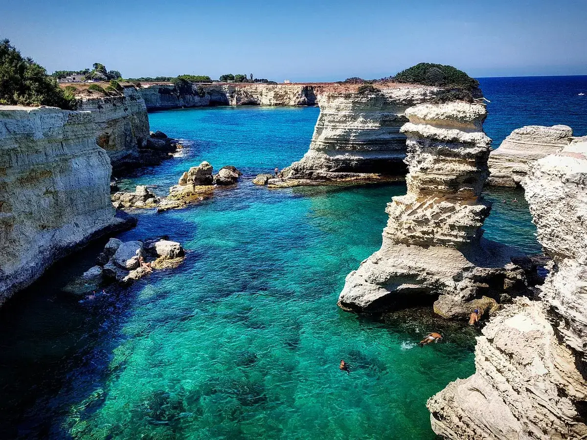 Turkost vatten och vita klippor vid kusten nära Lecce, Italien. Några badar i det klara vattnet.