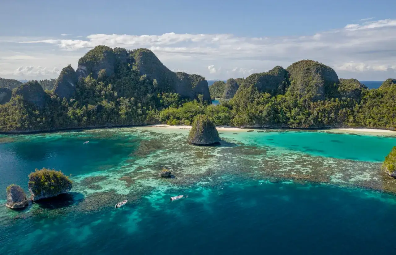 Drömlika öar med frodig grönska och turkost vatten vid Raja Ampat. Små båtar guppar vid korallreven.