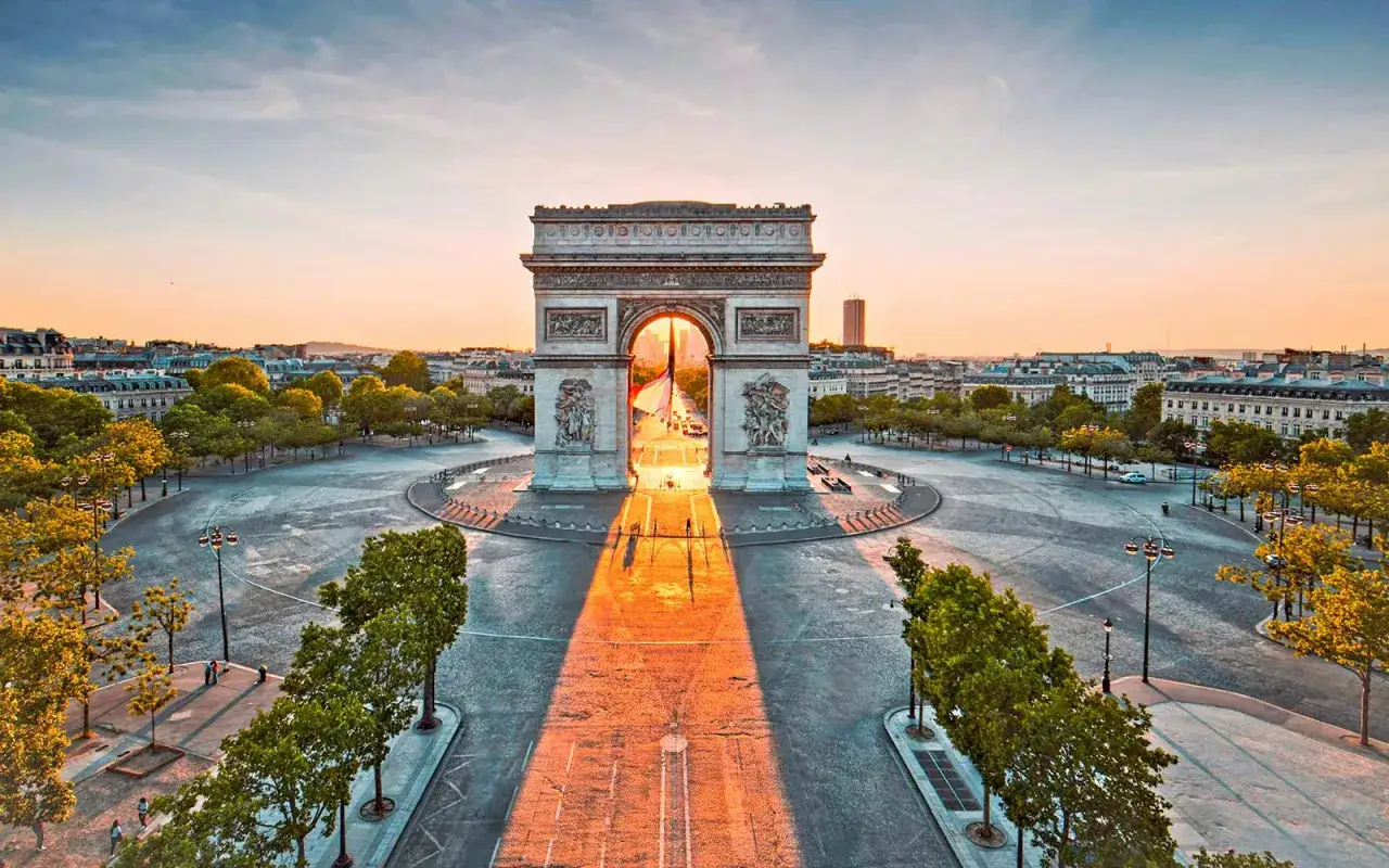 Parisisk morgonljus strålar genom triumfbågen. En ikonisk vy av Paris, med dess storslagna arkitektur och gröna träd.