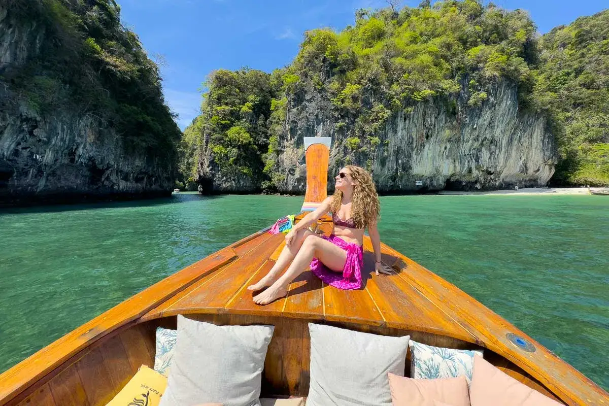 En kvinna njuter av solen på en träbåt i det turkosa vattnet vid Koh Hong, omgiven av gröna klippor.