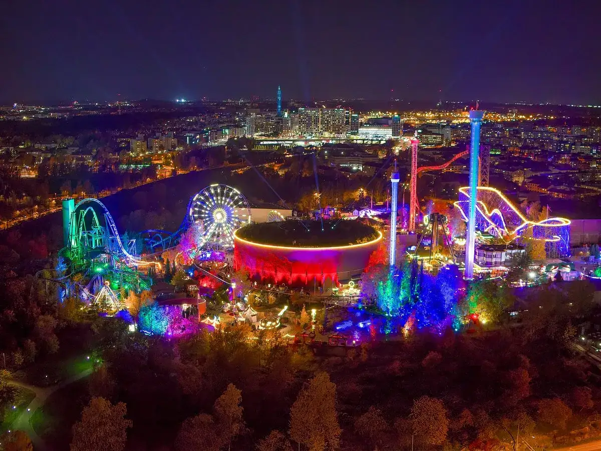 Nattbild över ett upplyst tivoli i Helsingfors med berg-och-dalbanor, pariserhjul och torn.