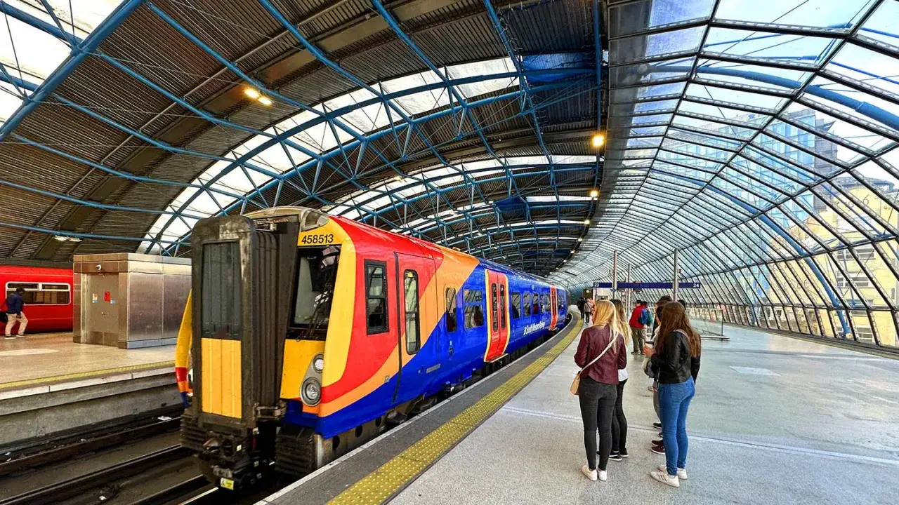 Färgglatt tåg redo för resan till London. Folk väntar på perrongen under den glasklädda takkonstruktionen.