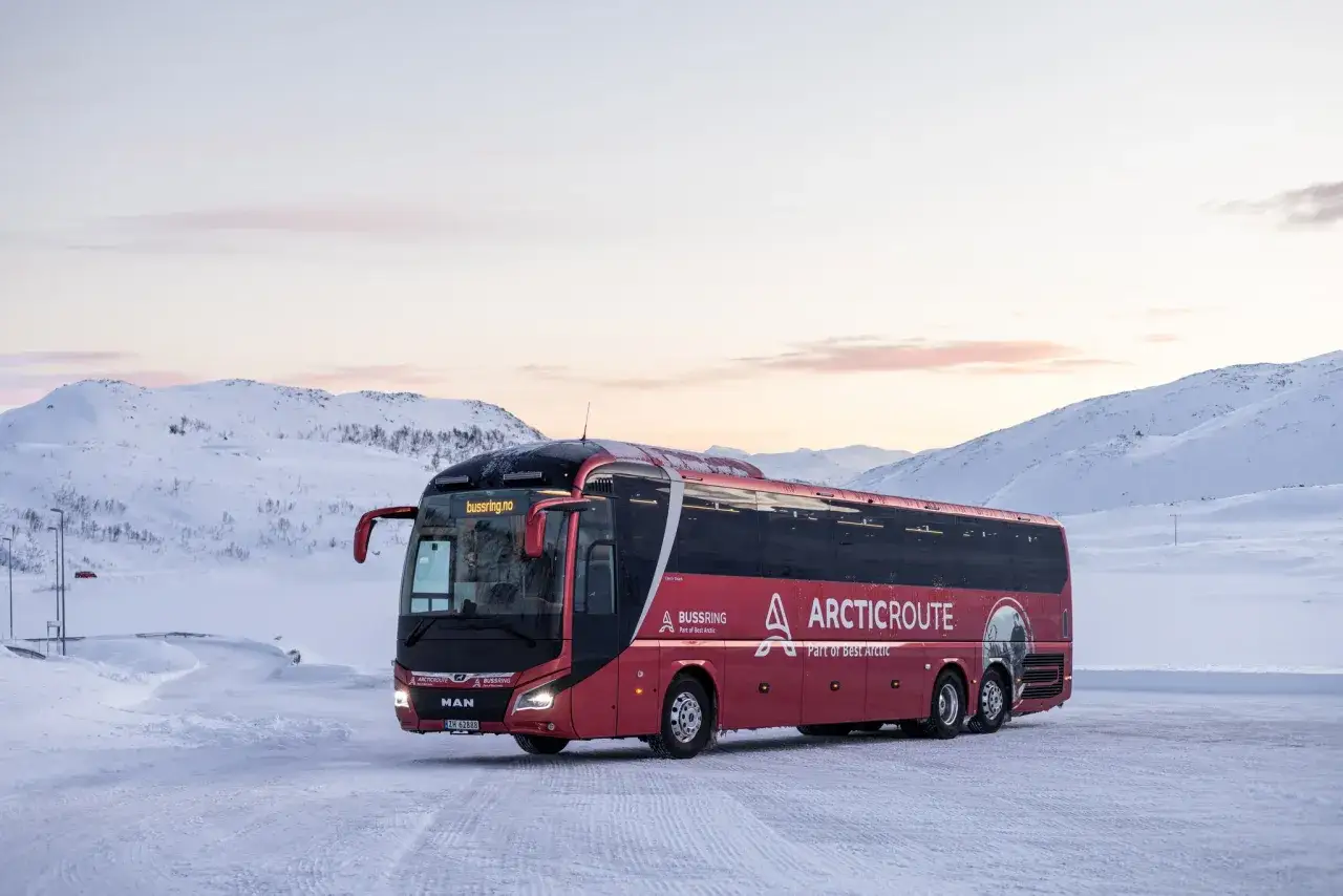 Röd buss från Arctic Route står parkerad i snölandskap. Kanske är det här resan börjar för en tåg till Lofoten-upplevelse.