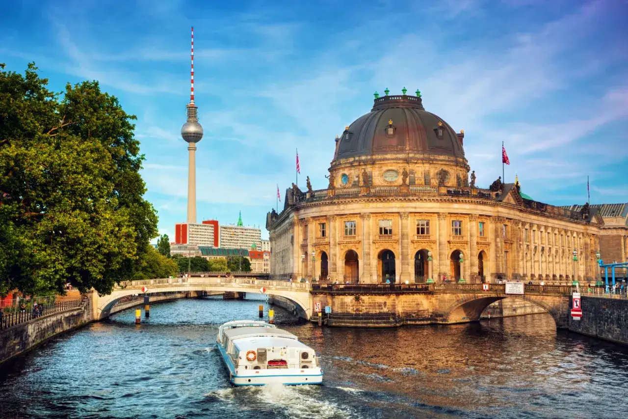 En båt glider fram på Spree, förbi Bode-museet och Fernsehturm. En perfekt vy för din berlin reseguide.