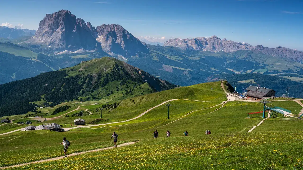 Vandrare njuter av den vackra utsikten i Val Gardena. Grönskande kullar, gula blommor och majestätiska berg.