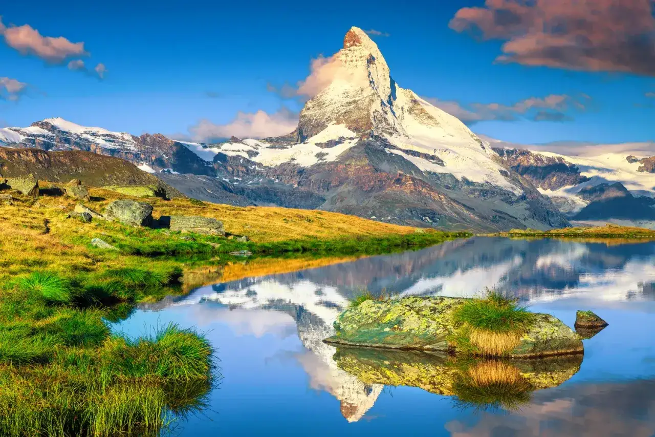 Vandra i Europa: Majestätiska Matterhorn speglas i en lugn alpinsjö, omgiven av gräs och stenar.