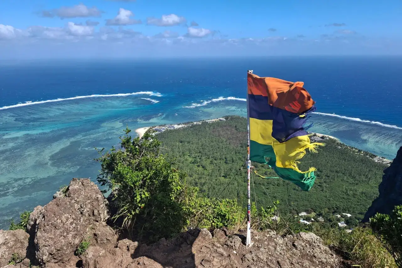En flagga vajar på toppen av Le Morne, med en fantastisk utsikt över turkost hav och frodig grönska.