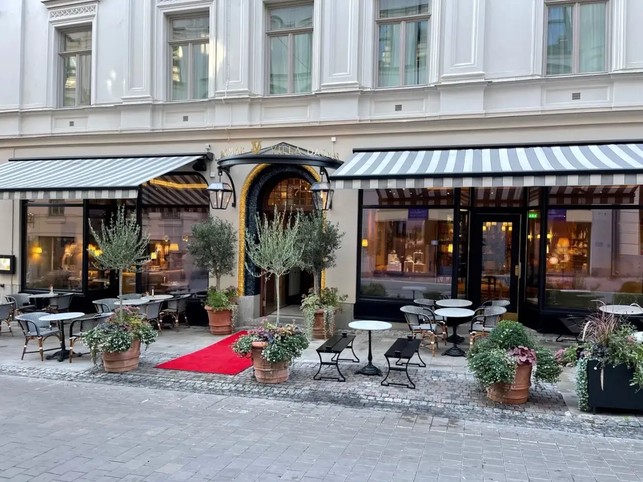 Elegant fasad med markiser och uteservering vid Dagmar restaurang. En röd matta leder till entrén.