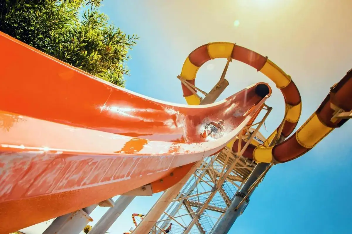 En person åker nerför en orange vattenrutschkana vid WaterWorld Ayia Napa. En gul och röd rutschkana syns i bakgrunden.