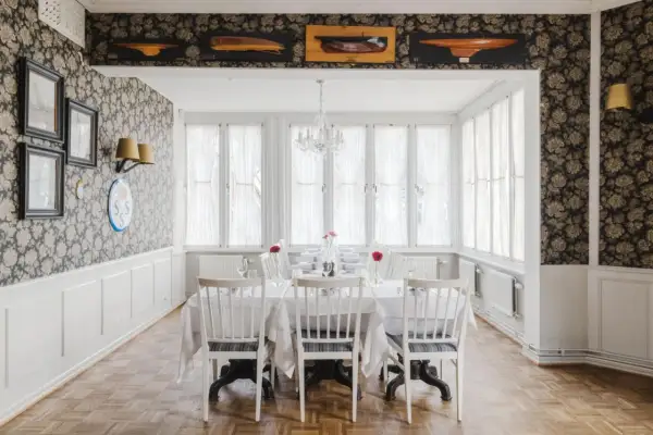 Elegant matsal med dukat bord, blommig tapet och modellbåtar i taket. Perfekt för en middag, som recensionerna för Villa Godthem antyder.