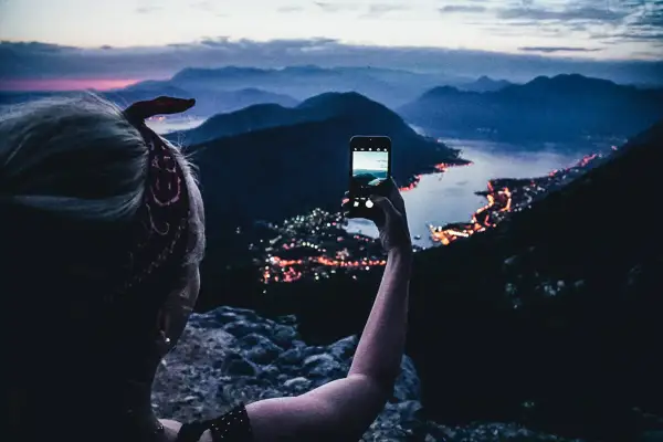 En person tar en bild med mobilen av en stad vid havet i Europa, med berg i bakgrunden.