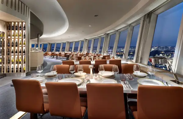 Elegant restaurang Berlin med utsikt över staden. Vackert dukade bord med glas och tallrikar. Vinhylla i bakgrunden.