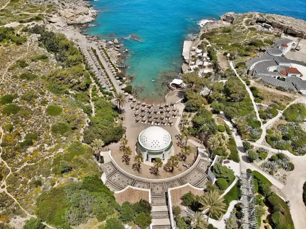 Vacker vy över Kallithea Beach med turkost vatten, solstolar och en kupolformad byggnad.