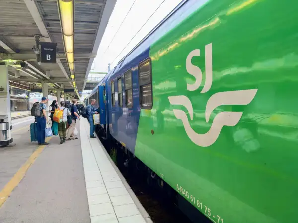 Folk väntar på perrongen vid ett grönt SJ-tåg, redo för en resa. Kanske är det ett tåg till London?